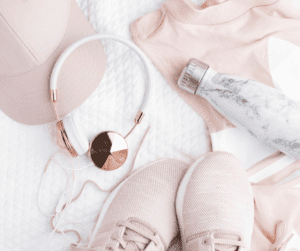 Image of rose coloured workout apparel such as a hat, running shoes, workout shirt, headphones and a marble water bottle. Showing the importance of drinking while exercising to help with dehydration and migraines. 