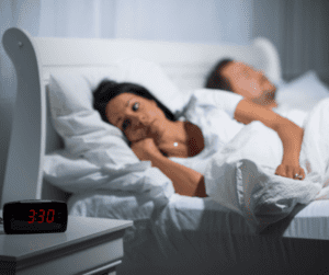 Image of a woman in bed awake and staring at an alarm clock showing 3:30am. 