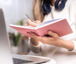 Image of a woman writing in a notebook showing using a migraine symptoms tracker to understand migraines at work. 