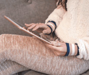 Image of a woman sitting on a couch with an ipad doing some mental brain teasers to help with addressing and learning how to combat what are the symptoms of fibro fog. 