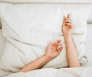 Image of a woman laying in bed with her hands up on the pillow showing the importance of sleep with fibromyalgia. 