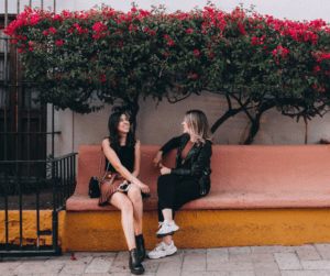 Image of two friends hanging out on a bench together. Showing making plans with friends despite invisible illness. 