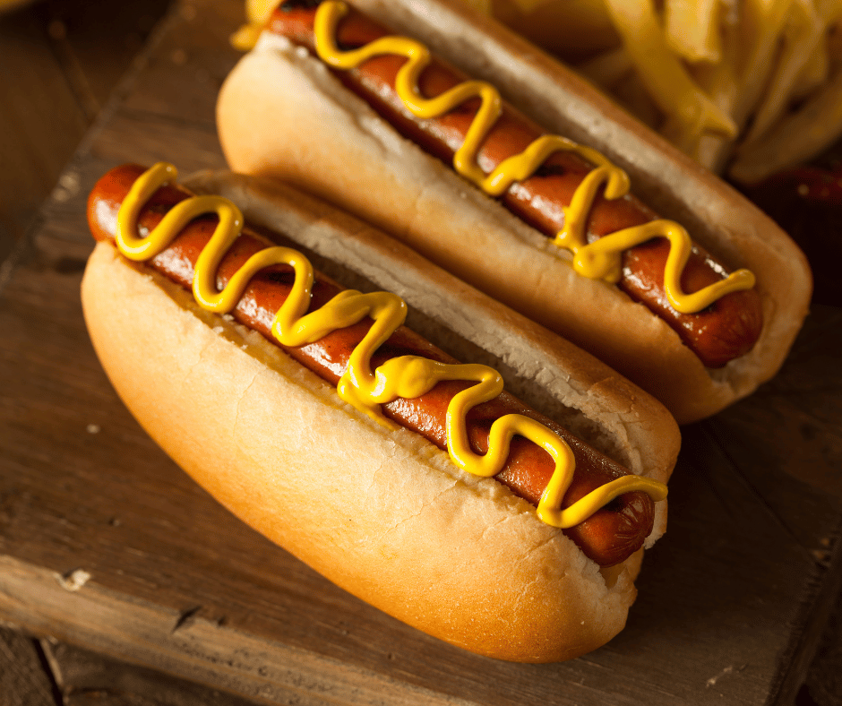 Image of hotdogs in buns with mustard ontop for foods that cause migraines. 