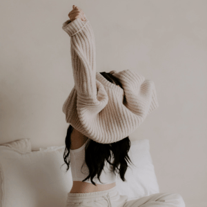 Image of woman getting dressed in the morning with fibromyalgia chronic condition. Putting a sweater over her head. 